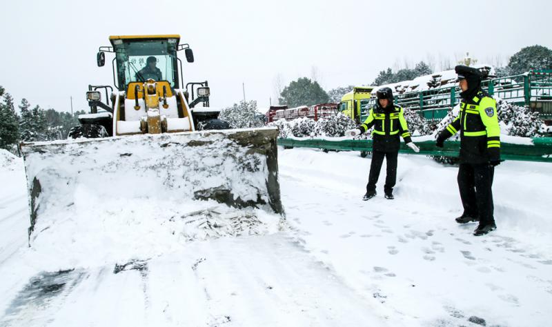 图:安徽省庐江县交警在指挥铲车清除道路积雪,为被大雪所困车辆扫清