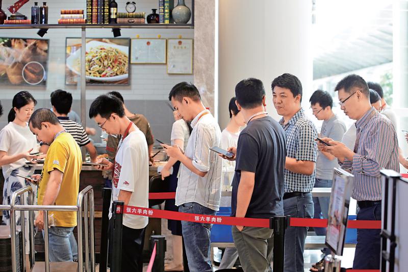 图:手机app吸引越来越多的人使用,图为在餐厅排队的人们看手机\资料